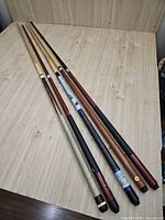Five assembled pool cues laid on table