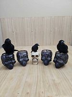 Front view of five skull candle holders with three crows displayed