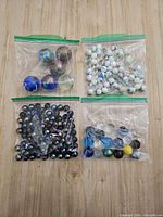 Four bags of mixed glass marbles on wooden surface