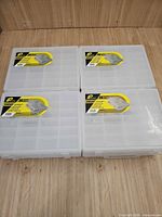 Four Plano clear organizer boxes showing lids with labels