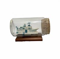 Side view of glass bottle on wood base showing origami ship