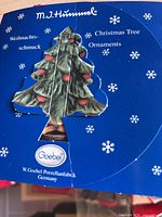 Front of blue Goebel M.I. Hummel display card with Christmas tree cut-out