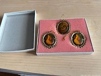 Open box showing three ornaments on pink foam insert