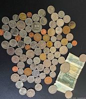 Full view of assorted coins and single banknote spread on black surface