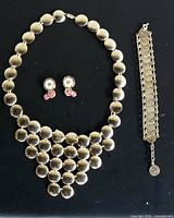 Necklace, earrings pair and bracelet laid out on black background