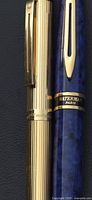 Close-up of Sheaffer gold ribbed pen beside Waterman blue marbled pen showing clips and upper barrels