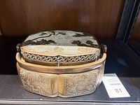 Angled view of closed brass trinket box displaying side engravings and lid