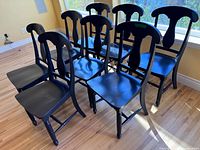 Eight black wooden chairs grouped together on hardwood floor