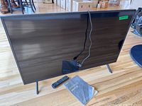 Front view of Samsung TV on stand with remote and manual visible