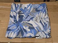 Folded blue/gray foliage pillow cover on box