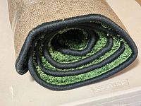 Rolled rug end showing green pile, black binding, backing