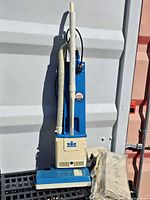 Full view of Windsor Versamatic upright vacuum cleaner with hose, wand and spare bags beside base