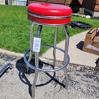 Full view of stool showing red seat, chrome legs and footrest