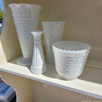 four milk glass vases on shelf showing shapes and patterns