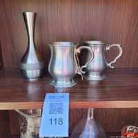 Front view of pewter vase and two tankards on shelf