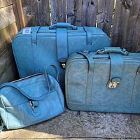Front view of all three light blue faux-leather luggage pieces