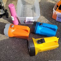Group of yellow, blue, orange lantern flashlights and pink torch on pavement