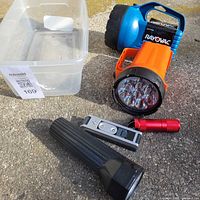 Group of four flashlights on pavement with clear bin, showing types and colors