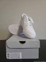 Pair of white Nike Air Force 1 sneakers on original grey shoe box, one shoe tilted to show sole pattern