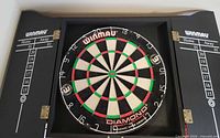 Dartboard mounted in black Winmau cabinet with scoreboards visible