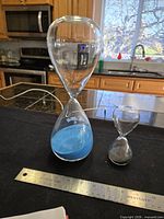 Both hourglasses side by side on table with ruler for scale