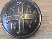 Front of brass button showing F A N Y cross design
