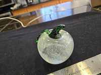 Oblique view of clear glass apple paperweight showing stem and internal bubbles
