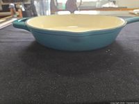 Side profile of teal enameled cast iron fry pan on black surface