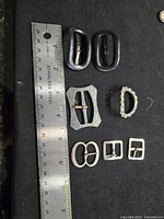 All eight buckles next to ruler for scale on black background