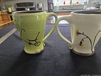 Pair of mugs showing handle side, bicycle and floral motifs visible
