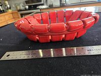 Side view of red ceramic woven basket with ruler showing scale
