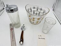 Group shot of ice bucket, shaker, mixing glass, opener with ruler for scale