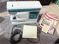 Front view of sewing machine, foot pedal, cord, and manuals