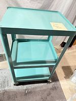 Full view of turquoise metal cart showing three shelves and casters