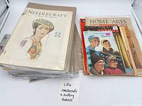 Stack of booklets in sleeves with Needlecraft magazine on top and several loose booklets beside
