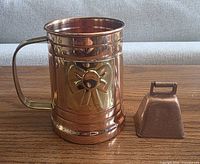 Copper mug with brass bow and small copper cowbell on wood table