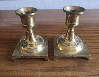 Pair of square-base solid brass candlestick holders showing design details and wear