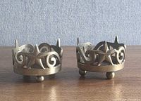 Two brass footed votive holders showing star and scrollwork design and three ball feet