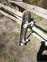 Full skateboard leaning on fence, showing bottom graphic, trucks and wheels