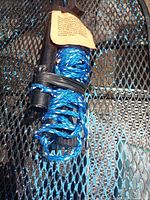 Coiled blue braided rope secured to black plastic handle with warning tag visible