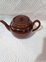 Side view of brown striped ceramic teapot showing handle and spout