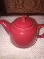 Side view of red ceramic teapot with lid and handle