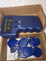 Handheld RFID writer and multiple blue keyfob tags inside box