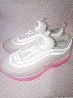 Lateral view of both sneakers showing beige upper, white overlays, pink sole