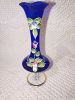 Full view of cobalt blue vase showing ruffled rim, floral enamel and pedestal base