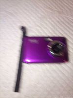 Front view of purple Vivitar Vivicam F128 camera with lens extended and wrist strap