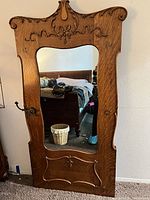 Front view of full-length oak cheval mirror showing frame, crest, mirror glass, lower panel, and brass hook