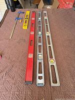 Five tools laid out: two silver Johnson 48" levels, one red 48" level, one yellow 24" level, one blue bar clamp