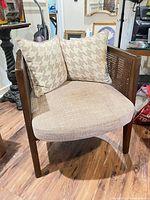 Front view of beige upholstered caned-back wood armchair with two pillows