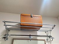 Front view of chrome wall-mounted coat rack with shelf, hooks, and reference object on top